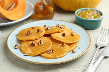 Tasty pumpkin pancakes with nuts, jam and honey on light grey table, closeup