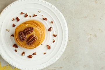 Tasty pumpkin pancakes with nuts and honey on light grey table, top view. Space for text