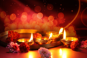 Diwali celebration. Diya lamps and beautiful flowers on color background, closeup. Bokeh effect