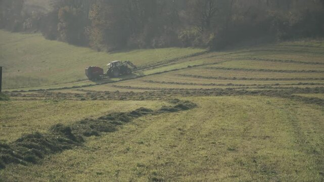 Tractor with hay baler or hay maker in the field in autumn, France