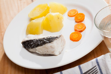 Steamed hake fillet served on white plate with boiled potatoes and carrot. Concept of diet food