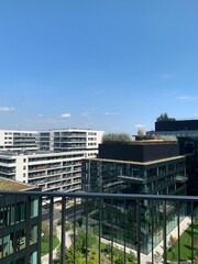 Obraz premium Contemporary urban buildings featuring glass facades and green rooftop gardens under a blue sky. Highlights sustainable architecture and modern city living. Ideal for themes of urban development and