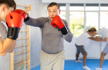 Adult man with partner in boxing gloves boxing in gym..