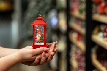 Red colored snow lantern with Santa in women's hands close-up.