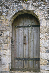 Old arched wooden door with metal fixtures in a stone wall, closse up