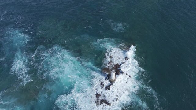 ripresa aerea di un faro in mezzo al mare durante una forte mareggiata , con le onde che si ingfrangono sugli scogli.