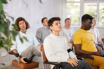 Group of focused men attentively listens to a lecture on same-sex relationships, sitting on chairs in the audience