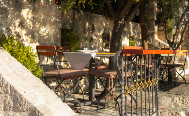 A charming outdoor cafe with a rustic table and chairs set under warm sunlight, offering a peaceful ambiance in a cozy courtyard surrounded by nature.