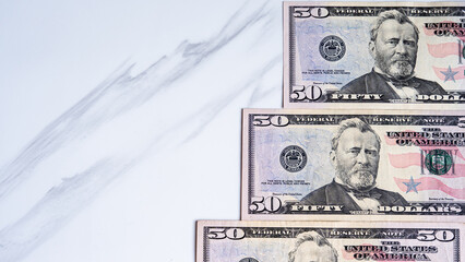 Fifty dollar bills arranged on a white marble surface