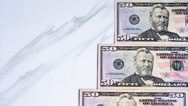 Fifty dollar bills arranged on a white marble surface