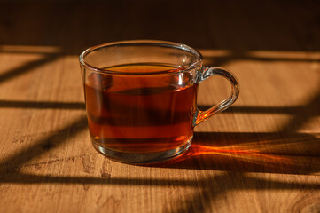 A beautifully illuminated glass of tea resting on a wooden surface in warm afternoon light
