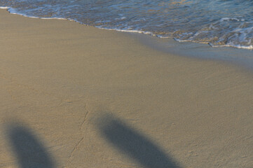 Footprints on serene beach sand beside gentle waves at sunset.