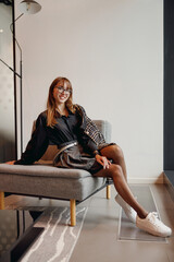 A trendy young woman relaxes on a stylish grey sofa, embodying modern fashion in a contemporary interior