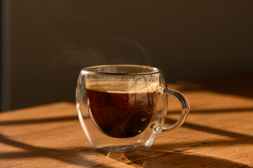 A steaming cup of coffee rests on a wooden table bathed in warm sunlight