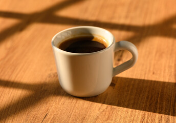 A cozy cup of coffee resting on warm wooden table in soft morning sunlight