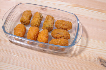 Chicken mushroom and cod croquettes arranged in a glass container on a wooden table