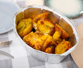 on wooden table, disposable baking dish with fried chicken breast and jacket-baked potatoes. Village food concept