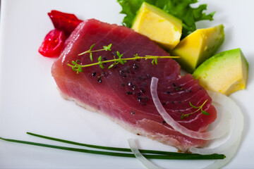 Delicious slightly fried tuna sprinkled with sesame served on white plate with avocado, sun-dried tomatoes and greens