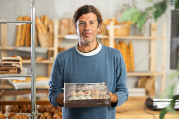 Positive middle-aged male customer standing in bakery shop with cookie box in hand