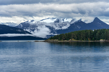 A forest island on calm sea water with a background of snowcapped mountains in Alaska