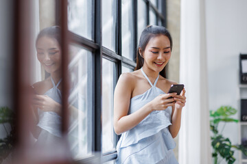 Cheerful beautiful Asian woman holding smartphone in the office workplace,
