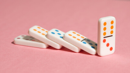 Domino tiles falling in a row on a pink background, illustrating the domino effect.