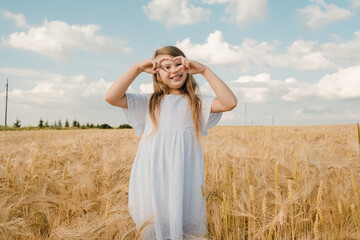 A beautiful girl in a wheat field shows a heart with her hands.