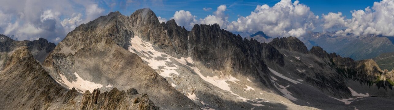 A wide panoramic shot capturing the rugged mountain range with patches of snow and rocky terrain, under a partly cloudy sky.