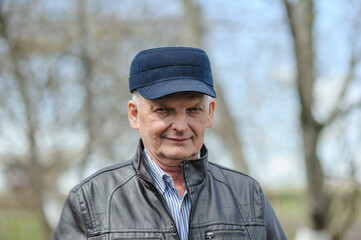 Happy man in his 60s. Old man in a blue cap standing in the park.