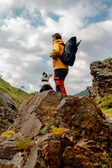 Male mountaineer with backpack, standing with his dog, on the rock of a mountain contemplating the landscape.