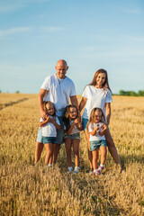 Mom, dad and  сute daughters hug in a wheat field. Beautiful children.Family vacation.Happy family resting in summer field.Cheerful family picnicking in the park.Summertime and vacation concept.