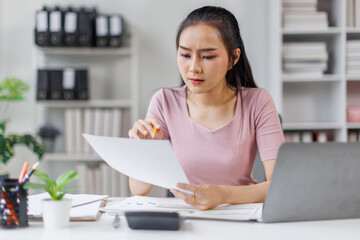 Asian Businesswoman Using laptop computer and working at office with calculator document on desk, doing planning analyzing the financial report, business plan investment, finance analysis concept.
