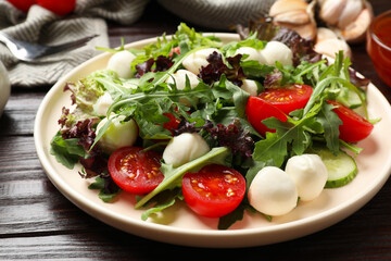 Tasty salad with arugula, lettuce, mozzarella cheese and vegetables on wooden table, closeup