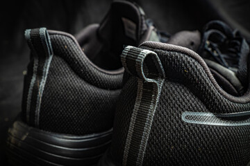 Detailed close-up of black athletic shoes set against a dark textured background in indoor lighting