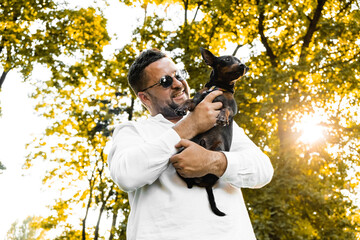Young man playing with his cute funny dog outside near the lake during beautiful sunset.