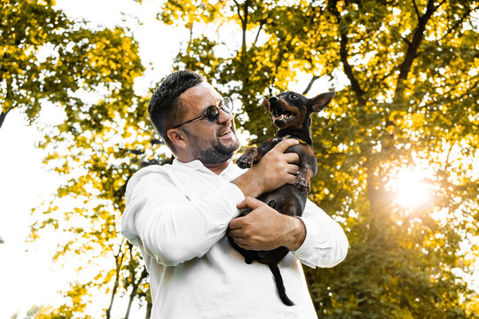 Black Man holds on his hands smiling  dog.Young man holding on hands his  dog, walking with cute puppy at summer day. - Powered by Adobe