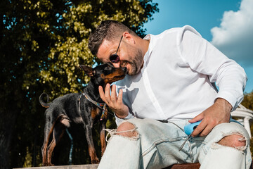 man walking with his cute dog at sunny day in city park.Cute dog outdoors walking and training in the park with his owner on a sunny day. Adorable puppy and his owner enjoying tim.