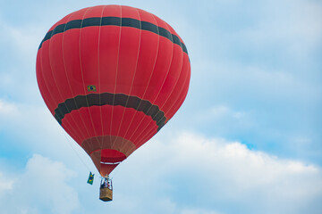 Naklejka premium Red hot air balloon with Brazilian flag flying against cloudy sky.