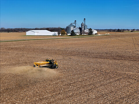 Self-propelled application vehicle spreading agricultural lime on a farm field to increase the soil's pH level. With farm scene in the background.