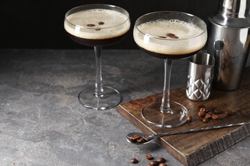Glasses of delicious espresso martini and coffee beans on dark textured table, closeup. Space for text