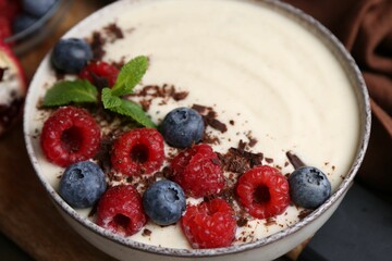 Tasty cooked semolina porridge with berries, chocolate and mint on table, closeup