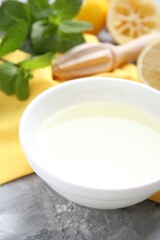 Fresh lemon juice in bowl, fruits, mint and squeezer on grey table, closeup
