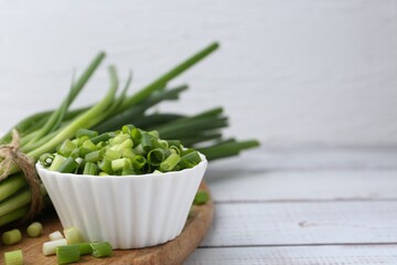 Chopped green onion in bowl and stems on white wooden table, closeup. Space for text