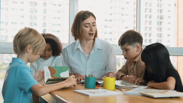 Professional caucasian teacher telling story to diverse student while sitting at table with storybook and colored book. Smart learner listening story while colored picture from instructor. Erudition.
