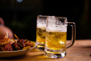 Two frothy pints of beer sit on a wooden bar counter, creating a warm, inviting pub atmosphere. Perfectly chilled with a golden glow, they evoke a sense of relaxation and camaraderie.