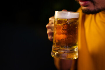 A man sits alone, holding a glass of beer, reflecting in quiet solitude. The golden drink shines, creating a warm, relaxed ambiance that invites moments of reflection and personal enjoyment