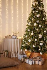 Christmas tree illuminated with lights and standing in front of white wall. Gifts in gift wrap under tree.