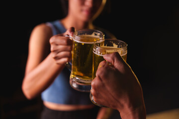 Close-up of friends clinking glasses of beer, celebrating together at a bar.The lively atmosphere captures laughter, camaraderie,good times, as young friends enjoy a night out with refreshing drinks