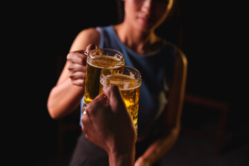 Close-up of friends clinking glasses of beer, celebrating together at a bar.The lively atmosphere captures laughter, camaraderie,good times, as young friends enjoy a night out with refreshing drinks