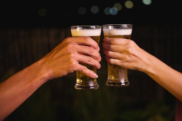 Close-up of friends clinking glasses of beer, celebrating together at a bar.The lively atmosphere captures laughter, camaraderie,good times, as young friends enjoy a night out with refreshing drinks